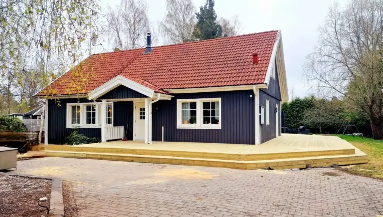 Mörkblått hus med rött tak och träaltan i grönskande miljö