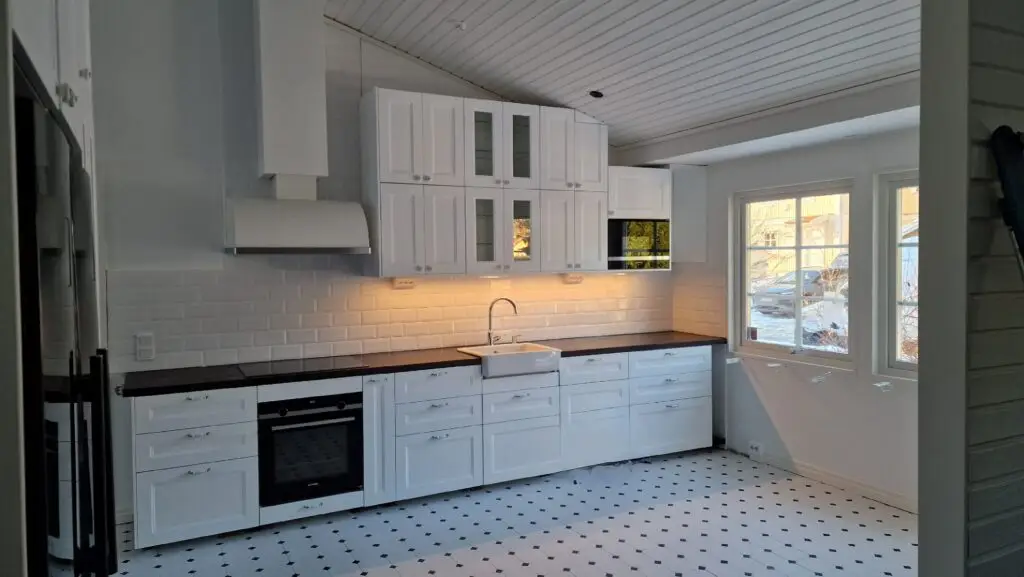 Nyligen renoverat modernt kök med vita skåp och mörk bänkskiva av Serving.nu