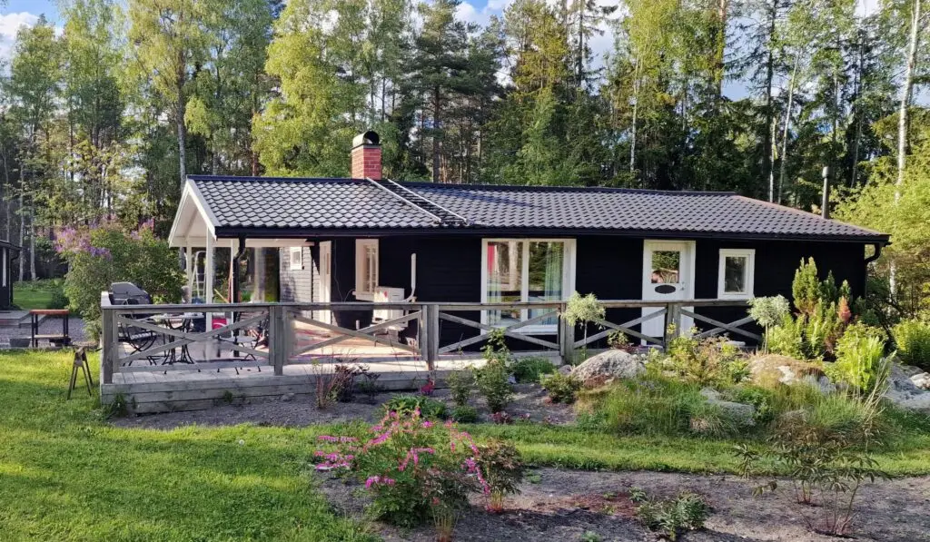 Svart trähus med nymålad fasad och tak, samt anlagd altan av Serving.nu